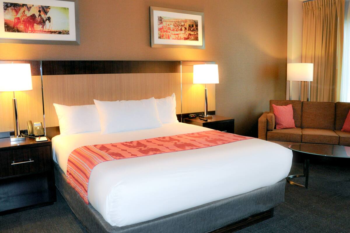 A hotel room with a large bed, two bedside tables, a sofa, and two lamps.