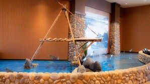 A pool area with a wooden swing bridge, rocks, and fish. - Legends Casino Hotel (Toppenish)