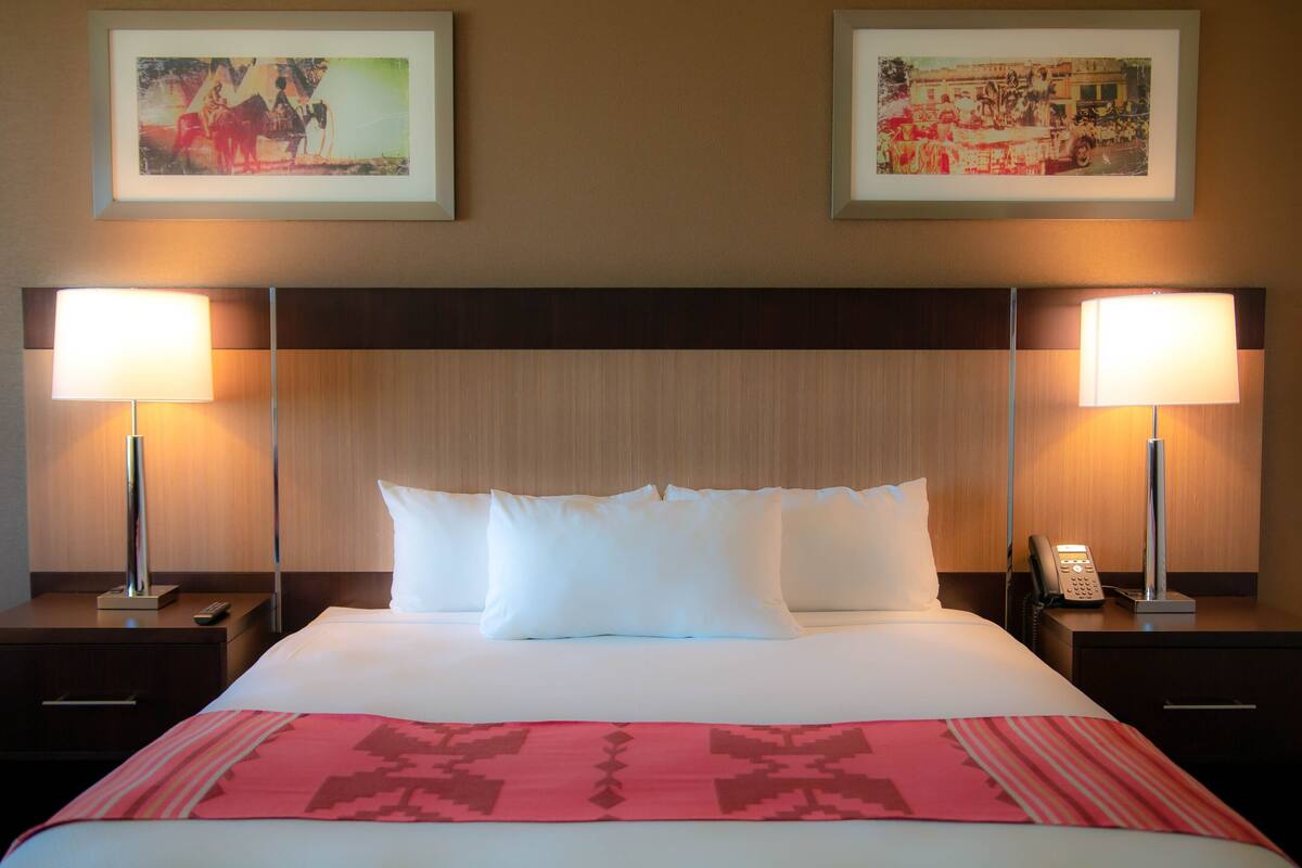 A hotel room with a large bed, two bedside lamps, a telephone, and two framed pictures on the wall.