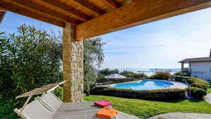 Uma área junto à piscina com vista para o mar, um espaço de estar coberto e um pilar de pedra.