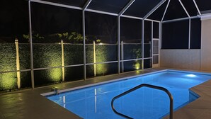An indoor swimming pool with a glass enclosure, surrounded by a hedge and a tiled floor.