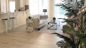 A spacious living room with a white sofa, a coffee table, and a dining area with chairs.