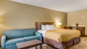 Una habitación de hotel con cama, sofá, escritorio y lámpara.