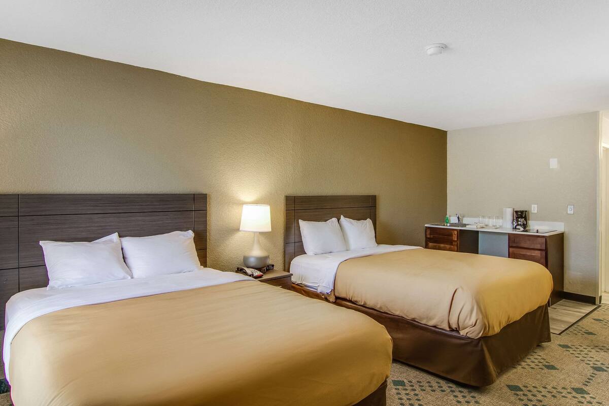 A hotel room with two beds, a desk, and a lamp.