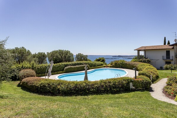 A swimming pool surrounded by well-maintained hedges, a clear view of the sea, and a building with a balcony. - Happiness: with lake view and pool (Toscolano-Maderno)