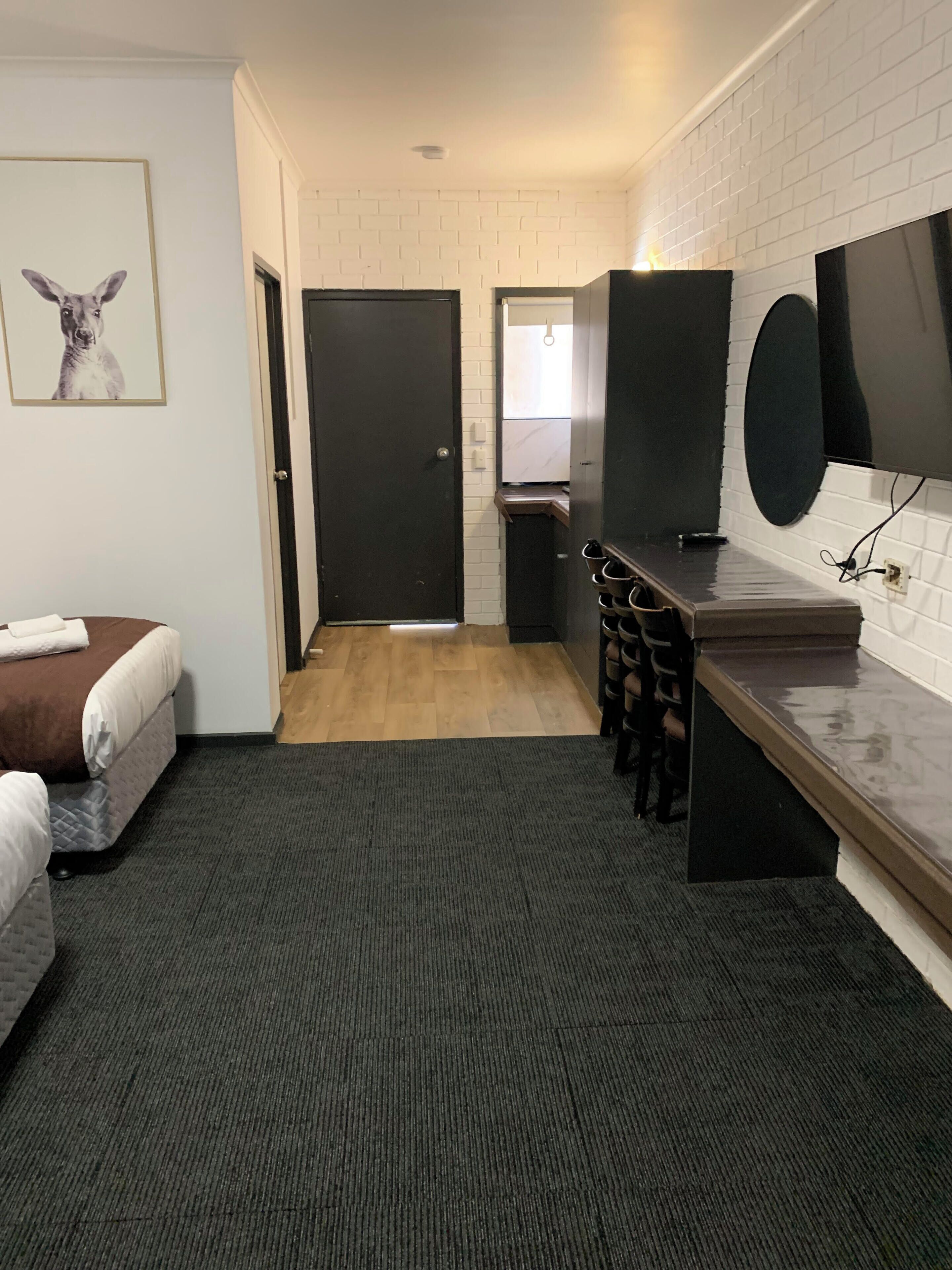 Ein kleines Hotelzimmer mit Bett, Schreibtisch, Spiegel und Fernseher.