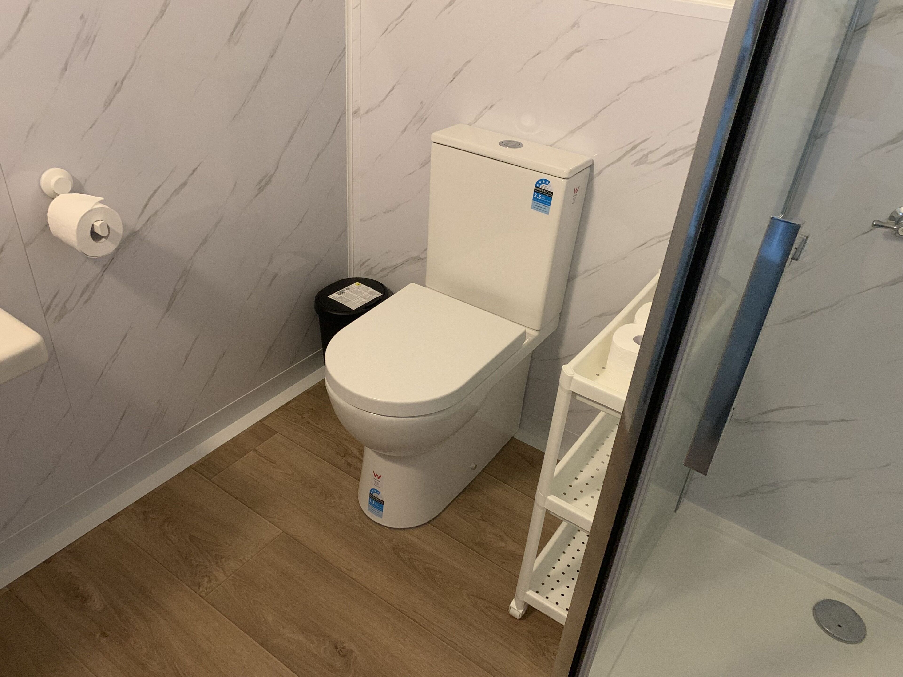 Un bany modern amb un vàter blanc, parets amb un disseny de marbre i un terra de fusta.