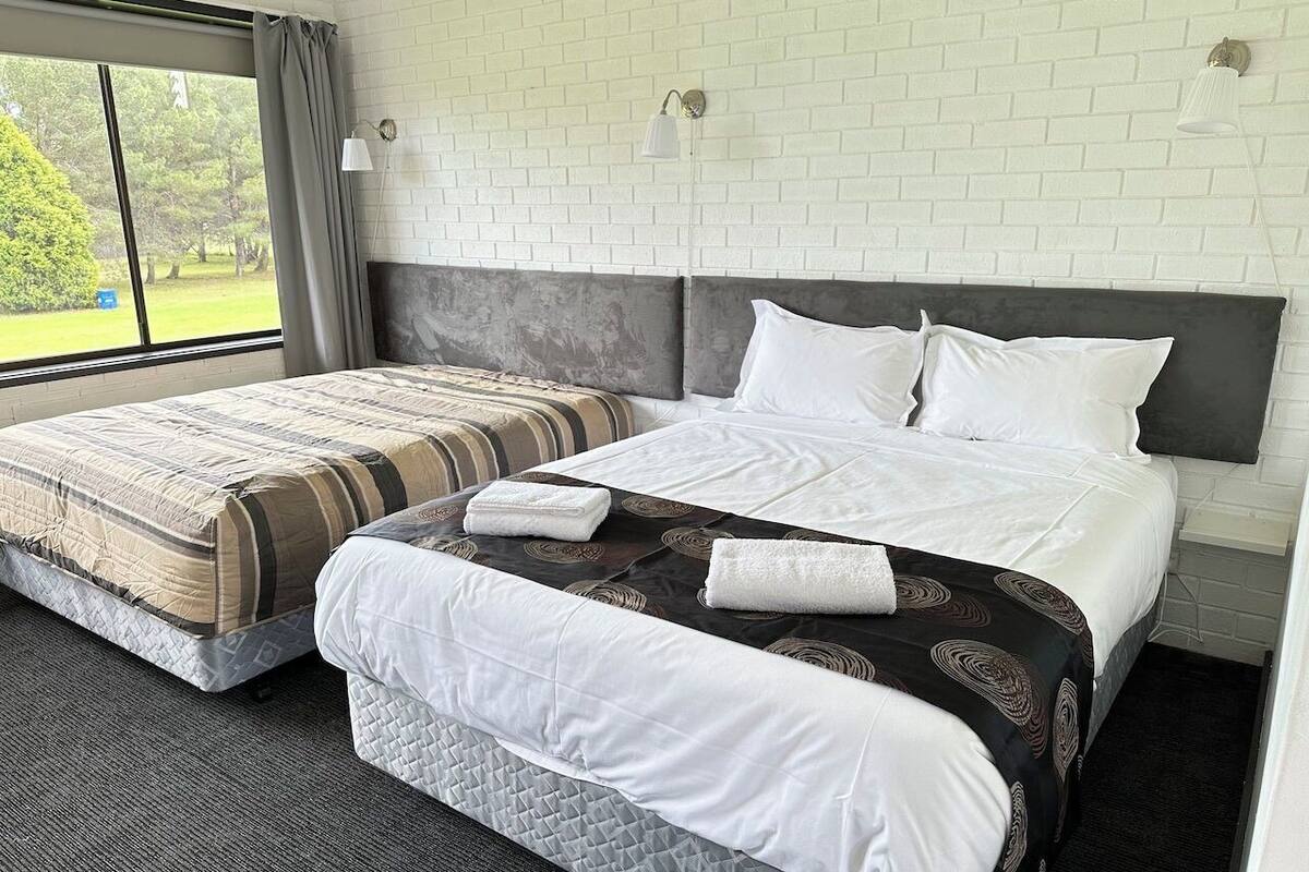 A hotel room with a large bed, a smaller bed, and a window with a view of greenery.