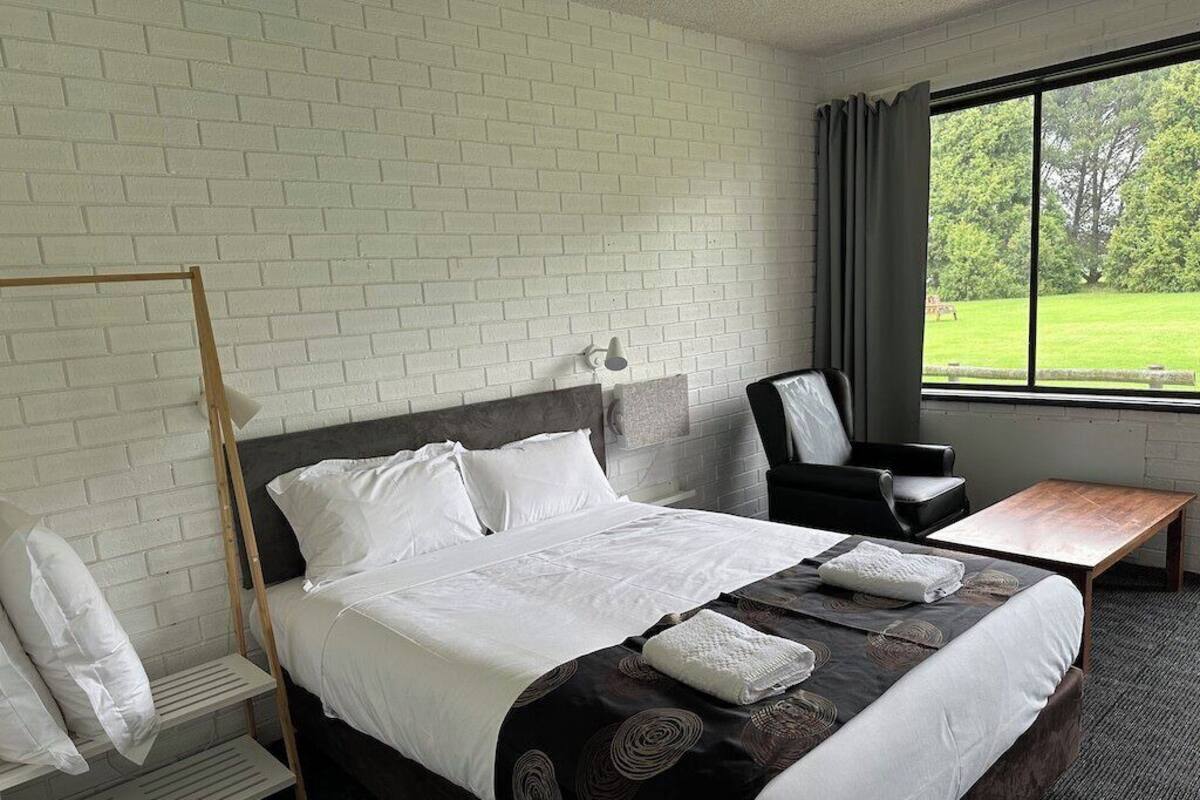 A hotel room with a bed, a desk, a chair, and a window with a view of greenery.