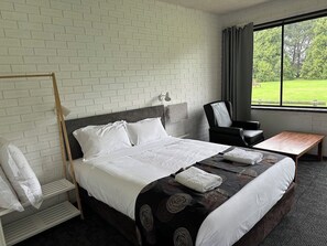 A hotel room with a bed, a desk, a chair, and a window with a view of greenery. - The Reserve Hotel (Sale)