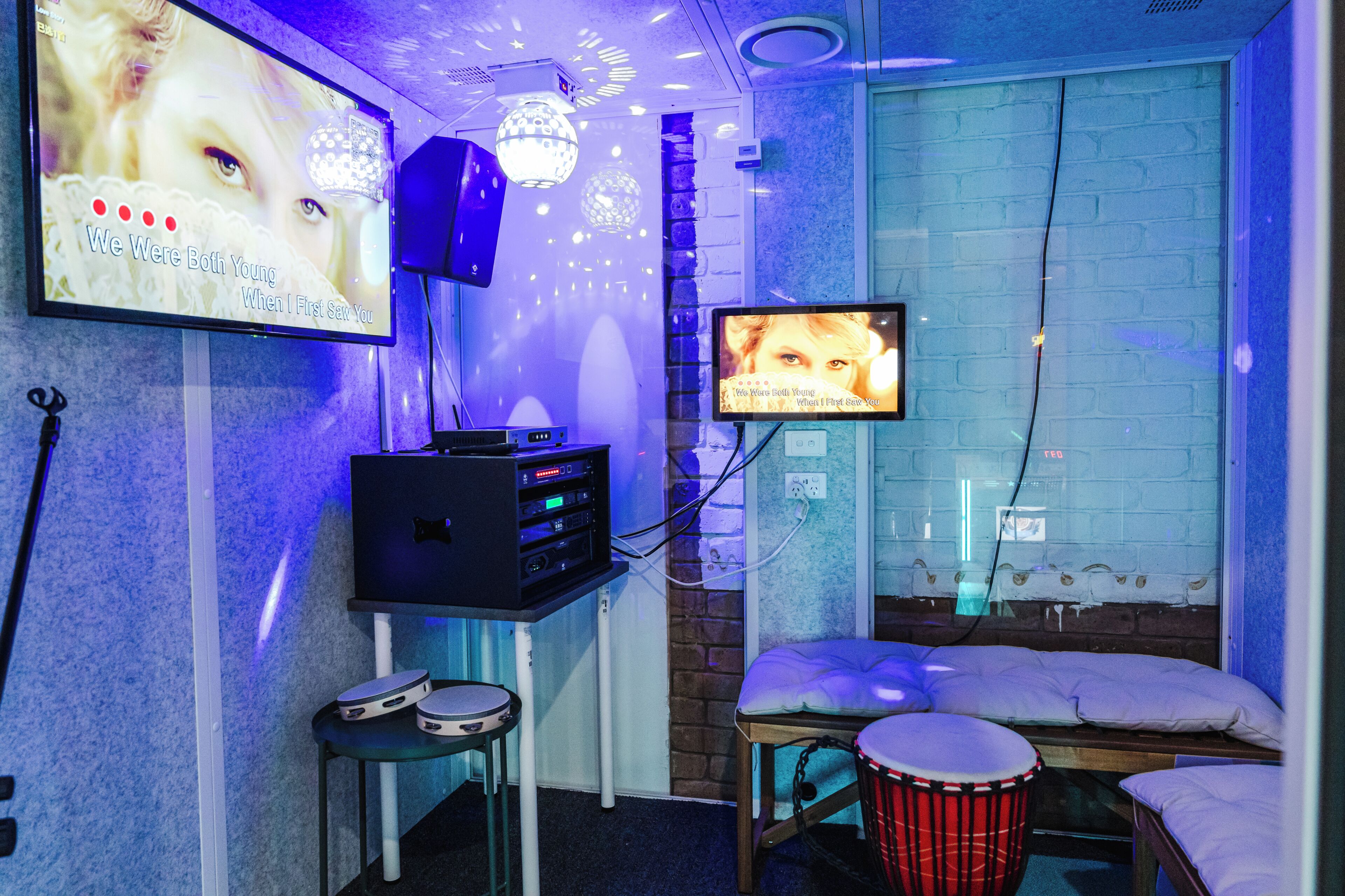 Una habitación con una cama, una batería, un altavoz y un televisor montado en la pared.