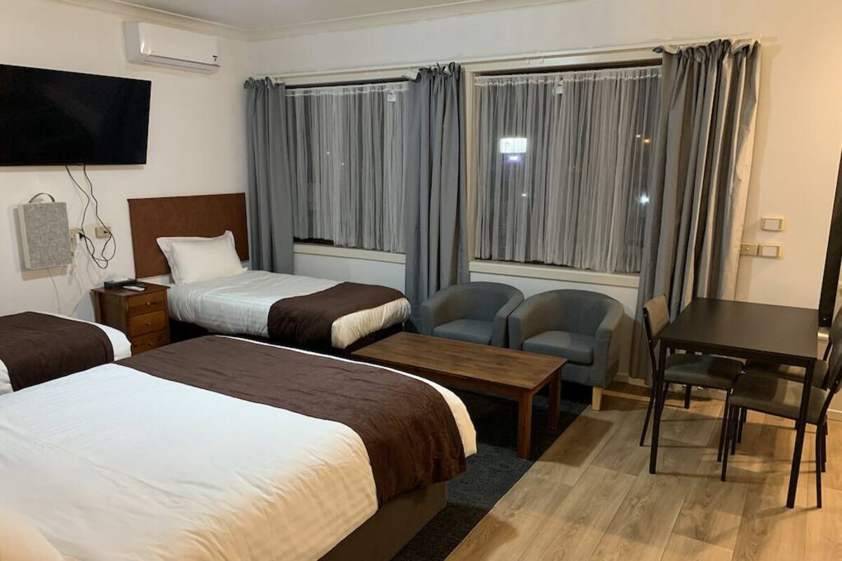 A hotel room with two beds, a desk, a chair, and a TV.