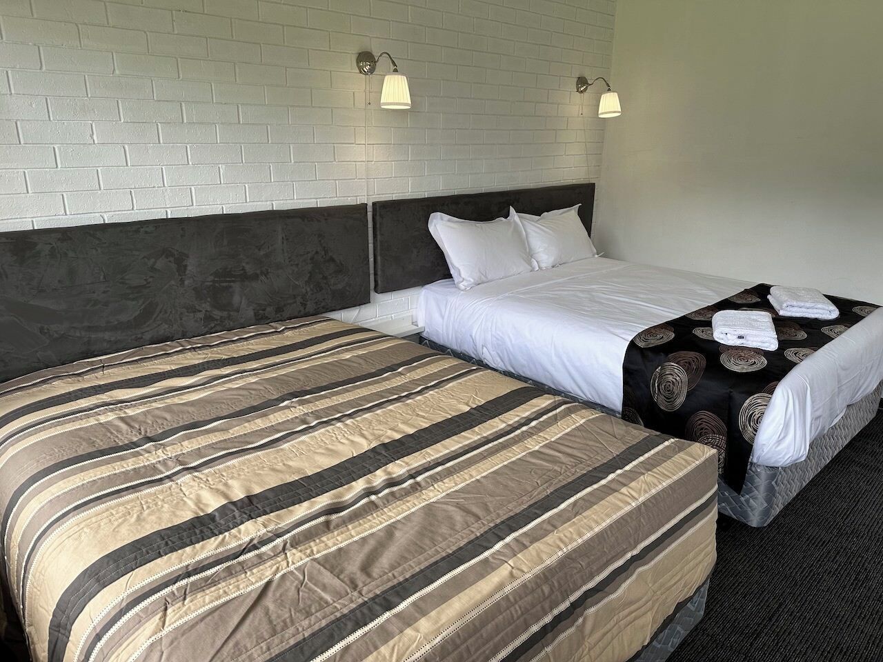 Una habitación de hotel con dos camas, una pared de ladrillos y dos lámparas fijadas a la pared.