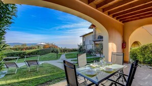 An outdoor patio with a glass table set for dining, surrounded by chairs, and a view of a building with a balcony.