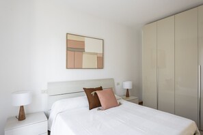 Habitación de hotel con cama, dos mesitas de noche, un armario y un cuadro abstracto colgado en la pared.