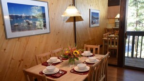 A dining area with wooden walls, framed pictures, a table set for six with white plates and red napkins, and a vase with flowers. - Beautiful Sleep 6 condominium at CLUB TAHOE, in Incline Village Nevada. (Incline Village)