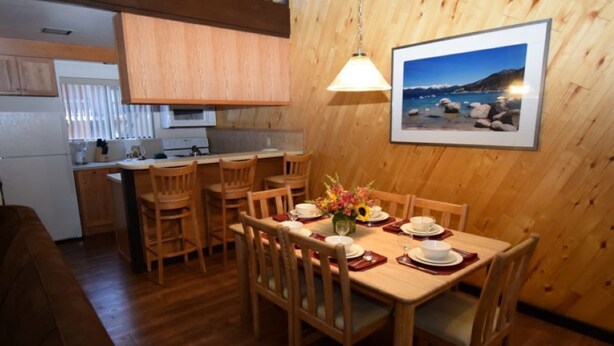 A wooden-paneled dining area with a table set for four, a kitchen in the background, and a framed picture on the wall. - Beautiful Sleep 6 condominium at CLUB TAHOE, in Incline Village Nevada. (Incline Village)
