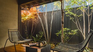 A patio with two black wicker chairs, a small table with a teapot, and a wooden floor. - Maana Kyoto (Kyoto)