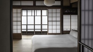 A traditional Japanese-style room with tatami flooring, a low bed, sliding shoji doors, and a hanging light fixture. - Maana Kyoto (Kyoto)