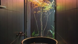 A bathroom with a large black bathtub, a wooden door, and a small shelf with a figurine. - Maana Kyoto (Kyoto)