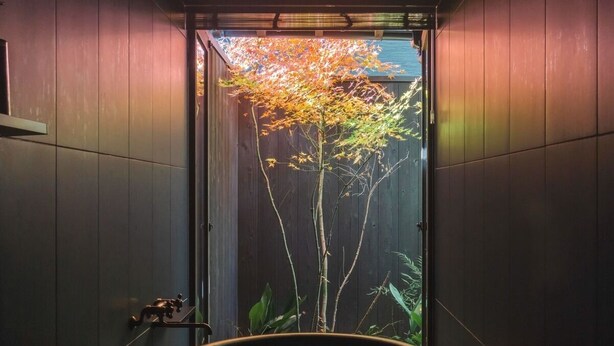 A narrow hallway with a large circular planter in the center, flanked by wooden walls and a door at the end. - Maana Kyoto (Kyoto)