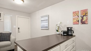 A modern kitchen with a dark countertop, white cabinetry, a coffee maker, and decorative wall art. - HC #102 xxxxxxxxxxxx (Austin)