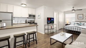 A modern apartment with a kitchen, dining area, and living room. It includes a microwave, stove, refrigerator, and a flat-screen TV displaying streaming services. - HC #102 xxxxxxxxxxxx (Austin)