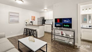 A modern apartment with a kitchen, living area, and a TV displaying streaming services. - HC #102 xxxxxxxxxxxx (Austin)