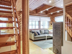 A cozy cabin interior with a wooden staircase, a sofa, and a stone fireplace. - Lomapykälä 1 a by Interhome (Kittilä)