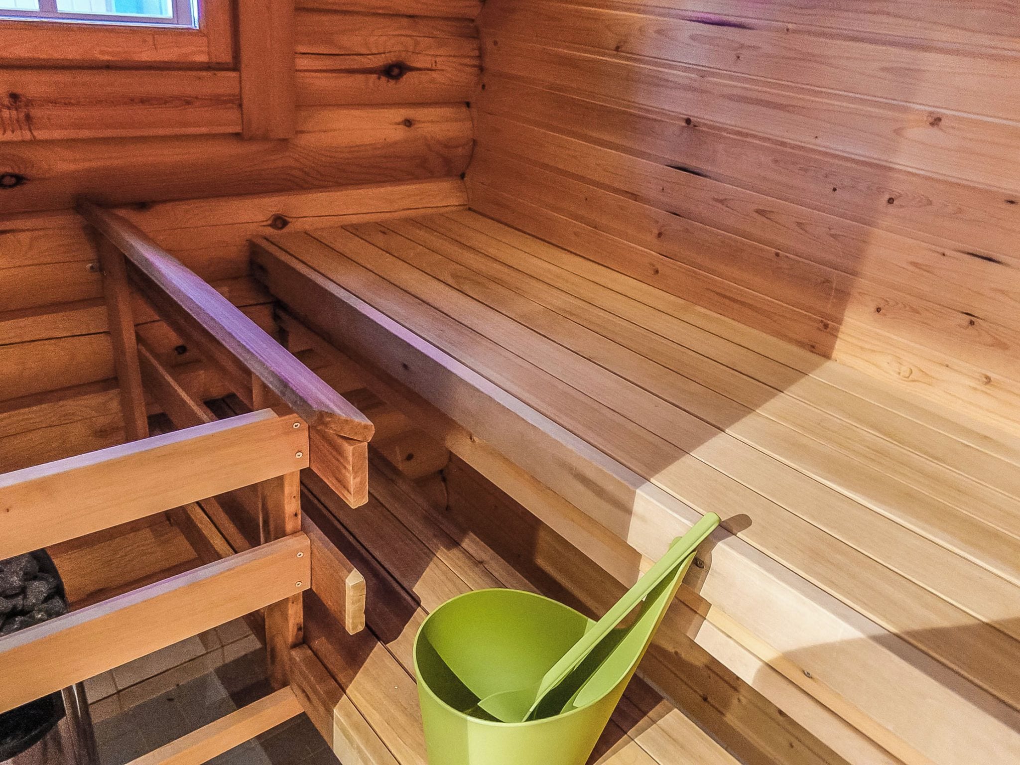 A wooden sauna with benches and a green bucket.