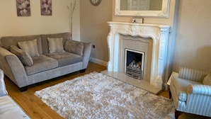 A living room with a grey sofa, a white fireplace, and a fluffy rug. - 4-bed House With Private Garden in Barnsley! (Barnsley)