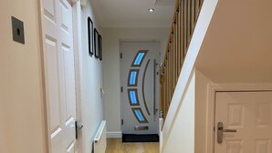 A hallway with a wooden floor, white walls, and a door with a window design. - 4-bed House With Private Garden in Barnsley! (Barnsley)