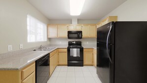 A kitchen with a black refrigerator, a black stove, a microwave, and wooden cabinets. - GATED 2 Bedroom/1.5 Bath Townhome FURNISHED  (Bakersfield)
