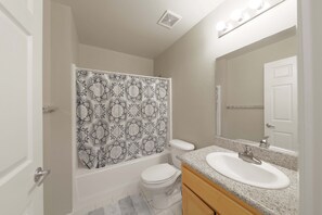 Ein Badezimmer mit Duschvorhang, Toilette, Waschbecken und Spiegel.