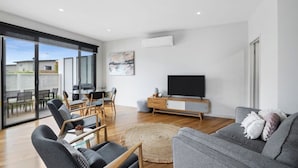 Una sala de estar moderna con un televisor de pantalla plana, un sofá gris y un comedor con sillas y una mesa.