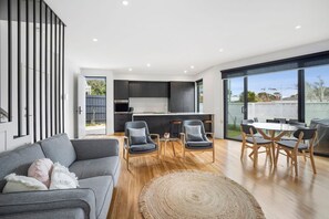 A modern living room with a grey sofa, a coffee table, and a dining area with wooden chairs and a glass table. - Spacious, Central to All Shops and beach (Torquay)