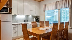 Una cocina compacta con armarios blancos, un microondas y una cafetera. Hay una mesa de comedor de madera con seis sillas.