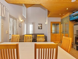 Un área de comedor con mesa y sillas, un sofá, una chimenea y un televisor montado en la pared.