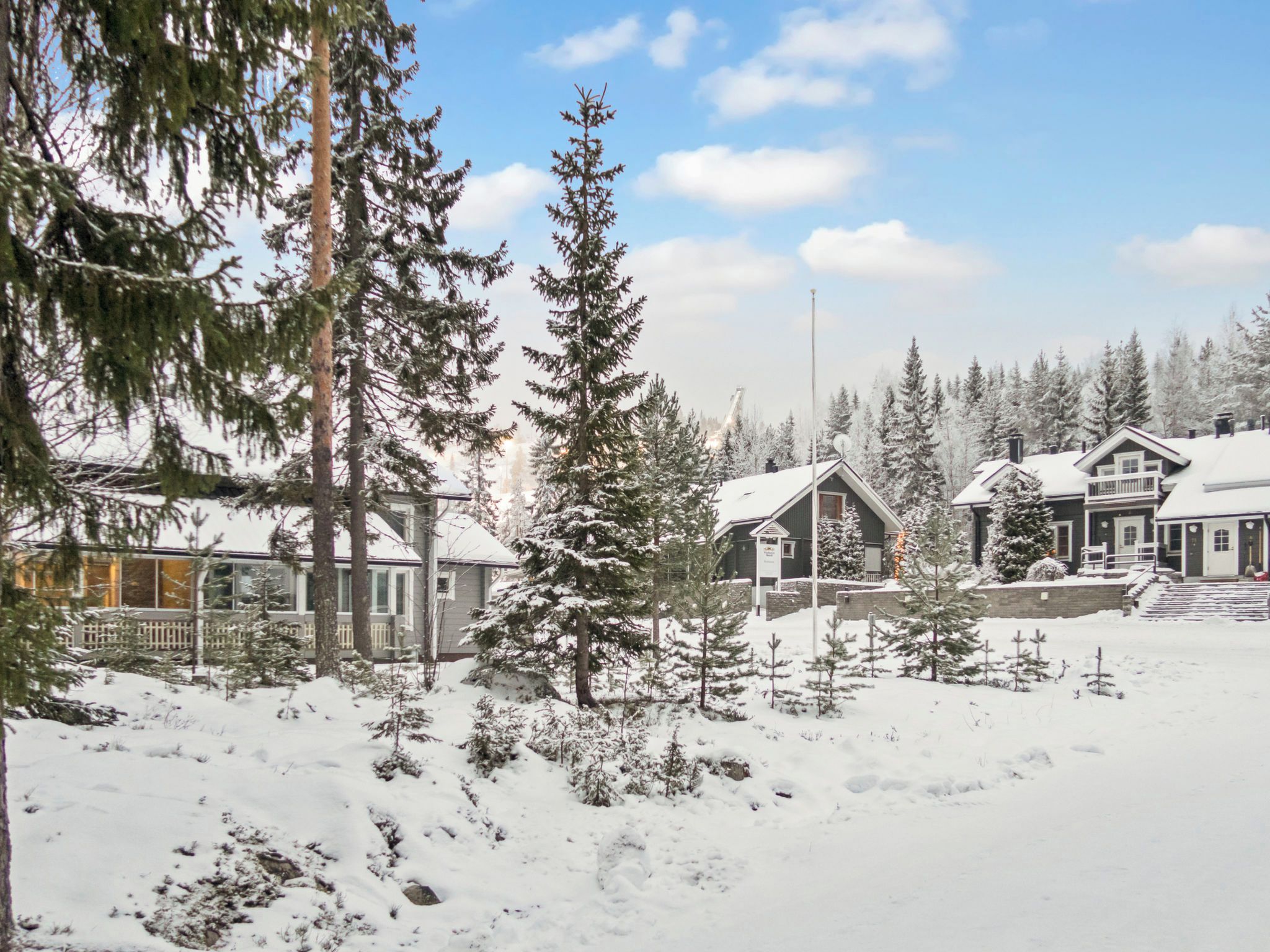 Lumipeitteinen maisema, jossa on taloja, puita ja kirkas taivas.