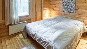 Una camera in una baita di legno, con un letto, una finestra con tende, un termosifone e un quadro appeso al muro.