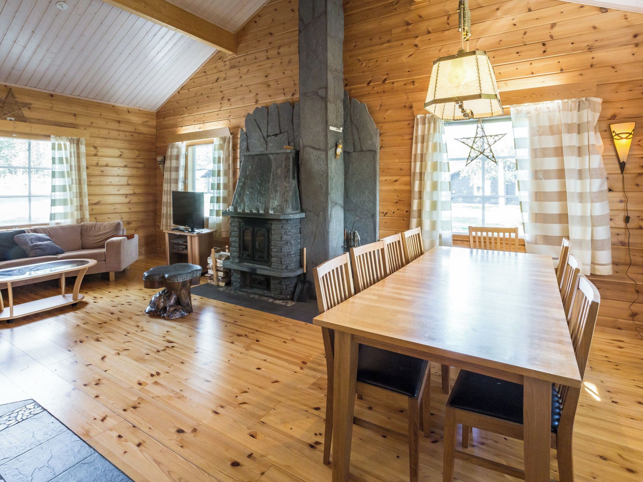 L’intérieur chaleureux d’un chalet avec une table à manger en bois, des chaises, un canapé, une cheminée et un téléviseur.