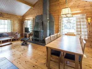 A cozy cabin interior with a wooden dining table, chairs, a sofa, a fireplace, and a television.