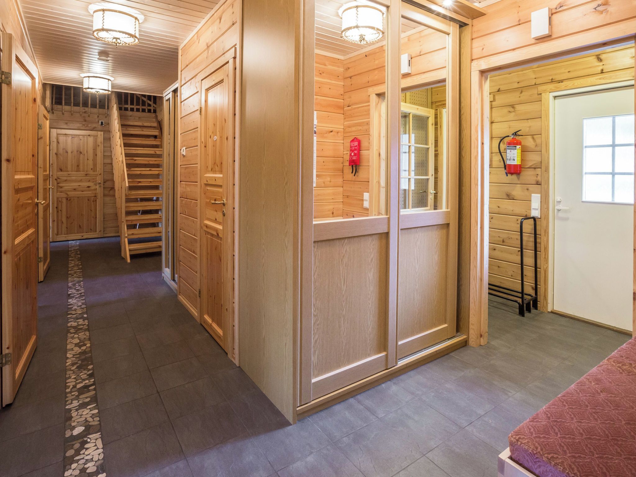 Un couloir intérieur en bois, avec un escalier, des portes et un extincteur.