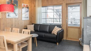 A cozy room with a wooden wall, a black sofa, a wooden dining table, and a window with a view of a building.