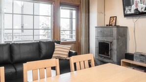 A cozy living room with a black leather sofa, a wooden dining table, and a stone fireplace.