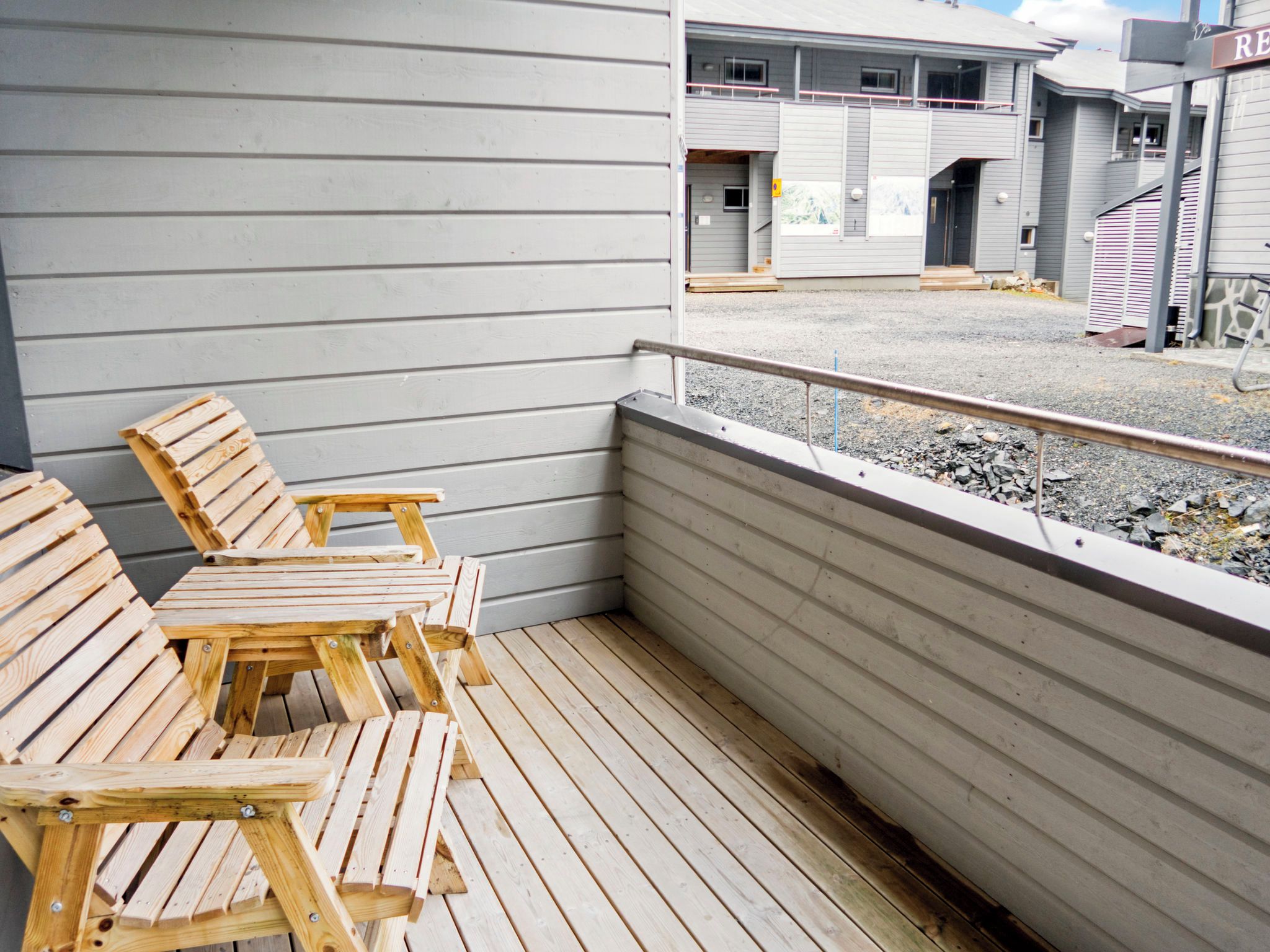 Eine Holzterrasse mit Sitzgelegenheiten und Blick auf ein Gebäude im Hintergrund.