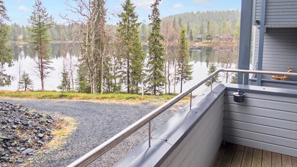 A balcony with a metal railing overlooking a lake surrounded by trees.