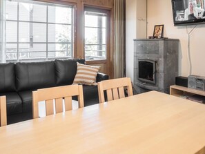 Un salon avec un canapé en cuir noir, des chaises en bois, une table en bois, une cheminée et un téléviseur fixé au mur.