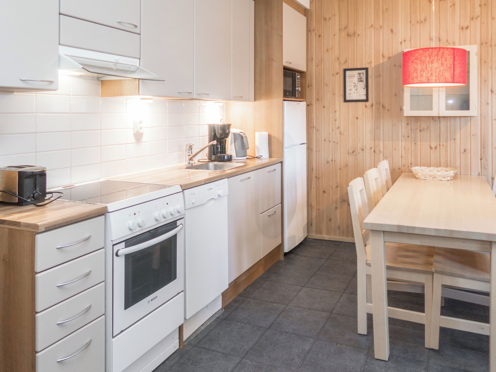 A modern kitchen with white cabinets, a Bosch oven, a coffee maker, and a wooden dining table with chairs.