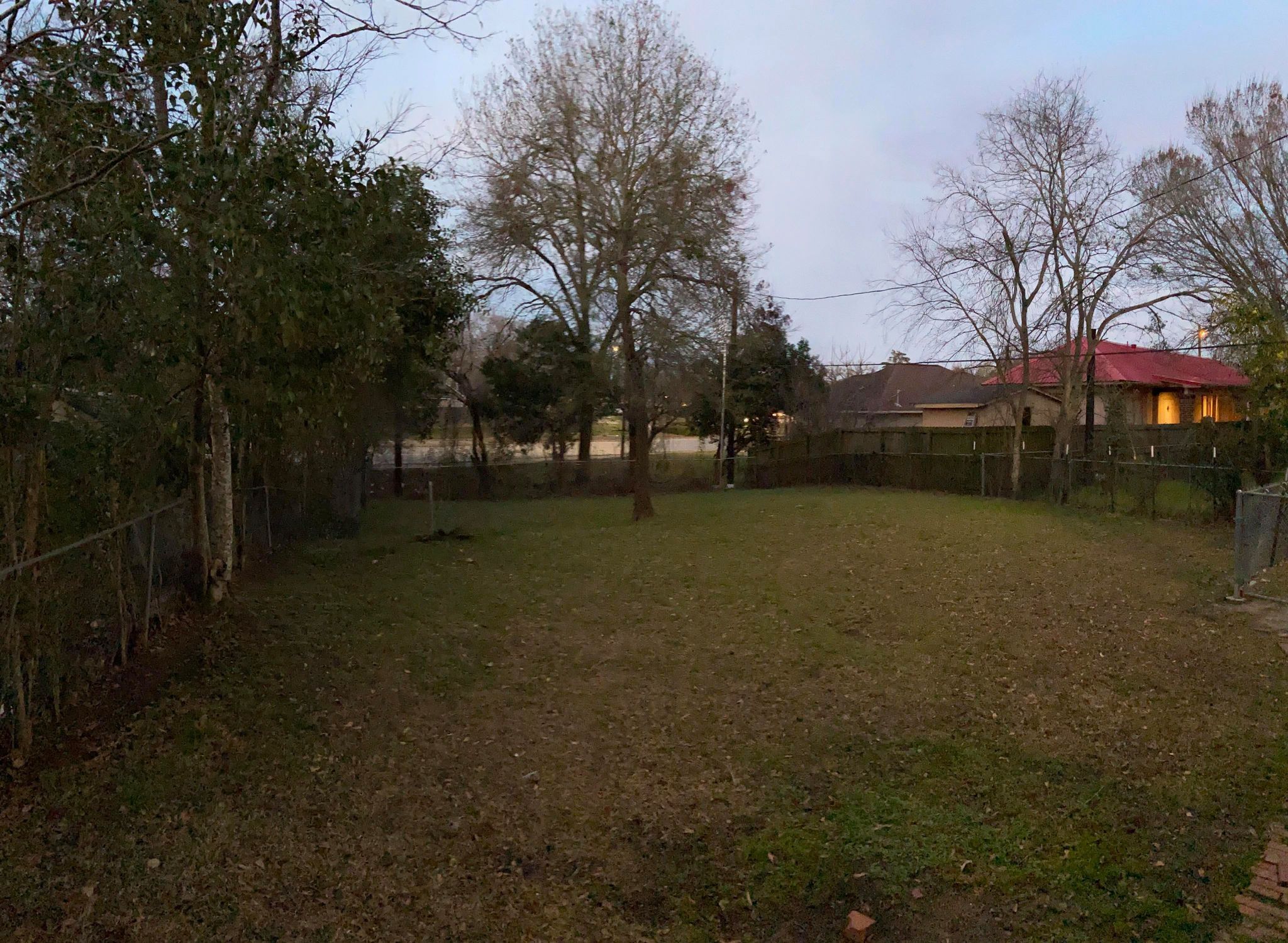Une cour arrière clôturée, avec des arbres et une maison en arrière-plan.